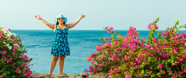 Photo a brunette woman in a blue sundress and hat among blooming bougainvillea stands