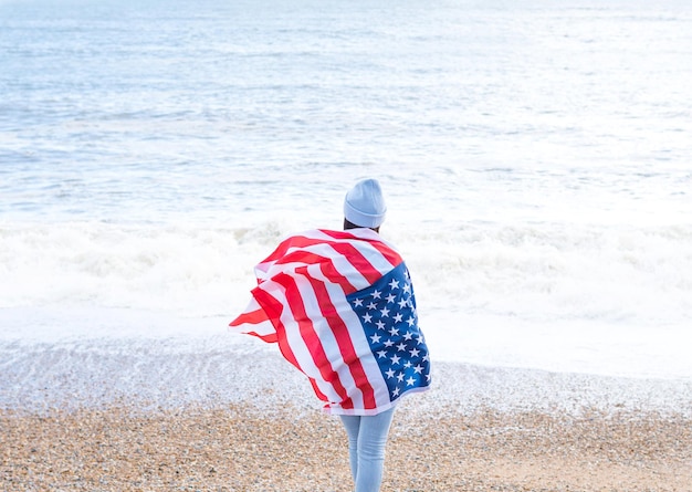 Photo brunette woman in blue sweater and hat with american national flag near sea