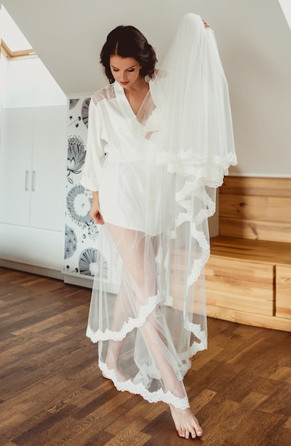 brunette woman bride in white silk robe preparing to wedding on white wedding dress background