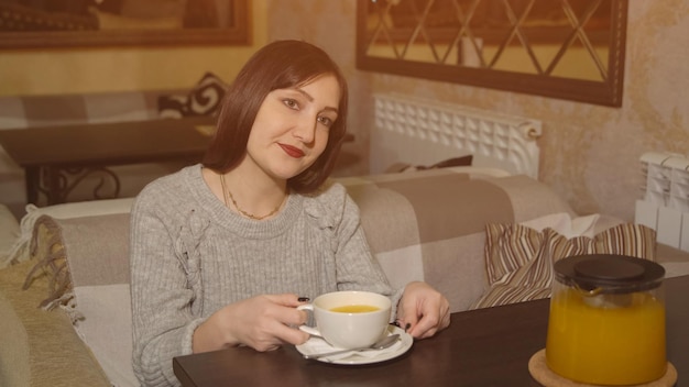 Donna castana in un caffè che beve tè alla vitamina, luce solare