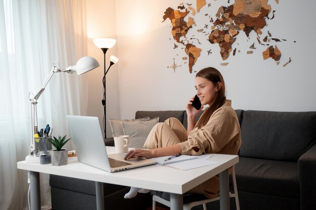 Brunette woman calling mobile and using laptop at table