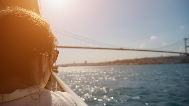 Brunette woman enjoys seascape traveling by boat in sea shimmering under sun rays close backside view