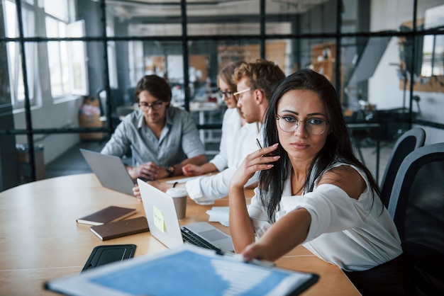 Brunette woman in front of employees. Young business people in formal clothes working in the office.