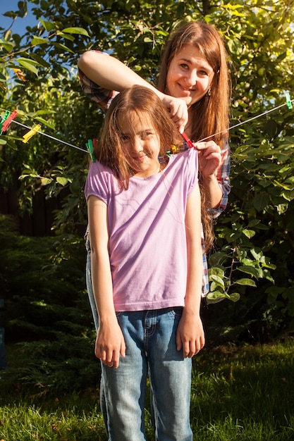 Brunette woman hanging girl on clothesline at garden