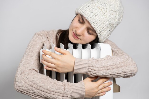 A brunette woman in a hat hugs an oil heater