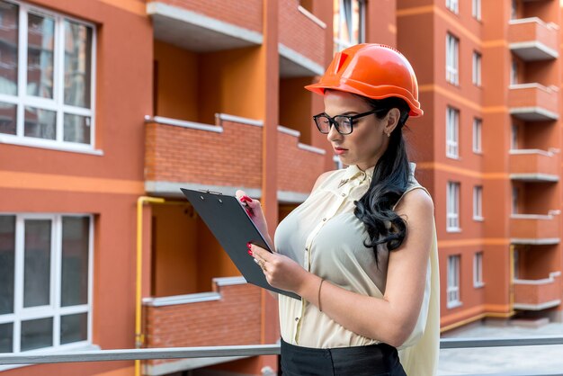 Brunette woman in helmet making notes on construction site