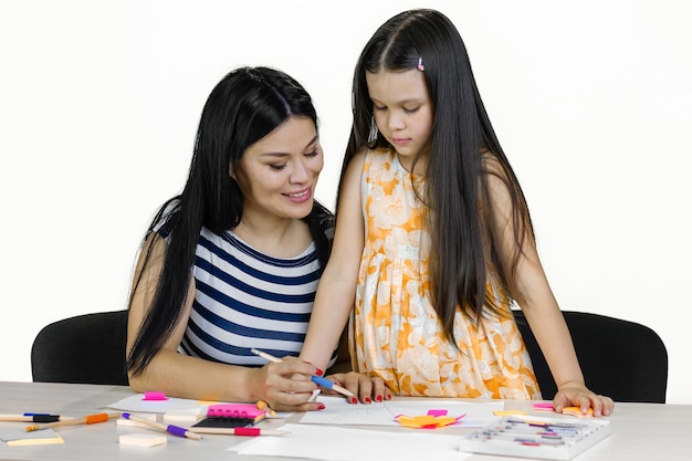 Brunette woman and her daughter at the desk are drawing something together isolated on white