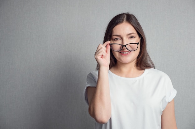 Brunette woman holds glasses on the tip of nose with one hand