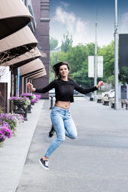 Brunette woman in jeans high jump on a city street