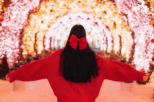 Brunette woman in a knitted cozy sweater and red bow in her hair against Christmas golden lights