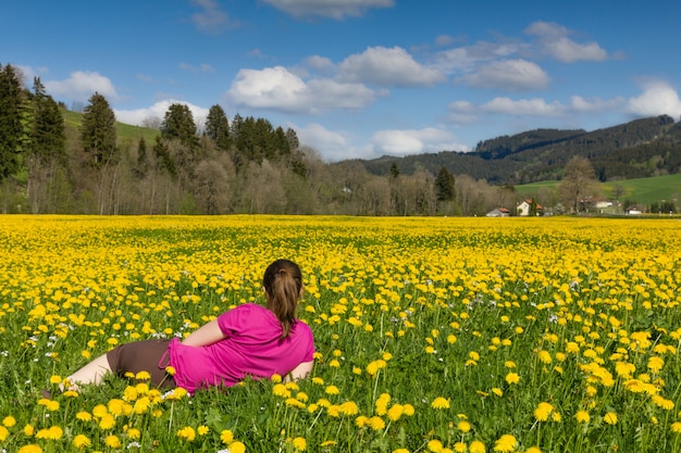 Photo brunette woman lies on a field of yellow dandelion.