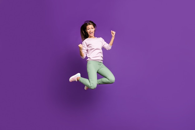 Brunette woman in pastel sweater posing against the purple wall