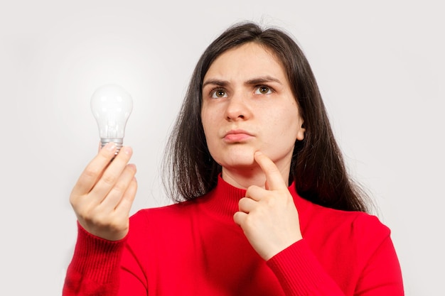 A brunette woman in red holds a glowing light bulb in her hand