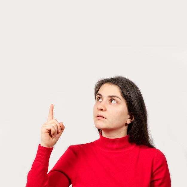 A brunette woman in red looks up and points her finger at a place for text.