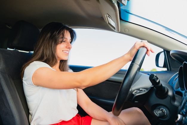 갈색 머리 여성은 자동차 살롱 안에 앉아 운전대를 잡고 운전을 하고 행복한 여성 운전자입니다.
