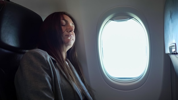 Brunette woman sleeping while sitting in an uncomfortable position on the plane.