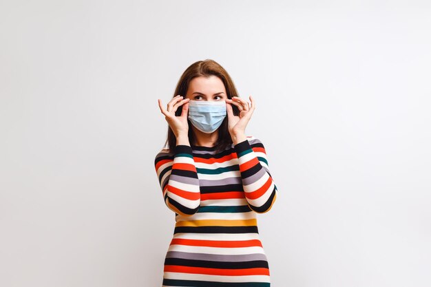 La donna castana in vestito multicolore a strisce mette sulla maschera medica concetto di protezione del virus