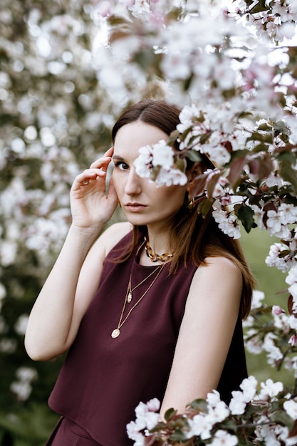 a brunette woman in a stylish suit stands near Apple trees in bloom on a warm summer day.