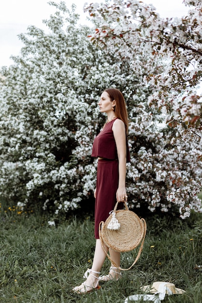 a brunette woman in a stylish suit stands near Apple trees in bloom on a warm summer day.