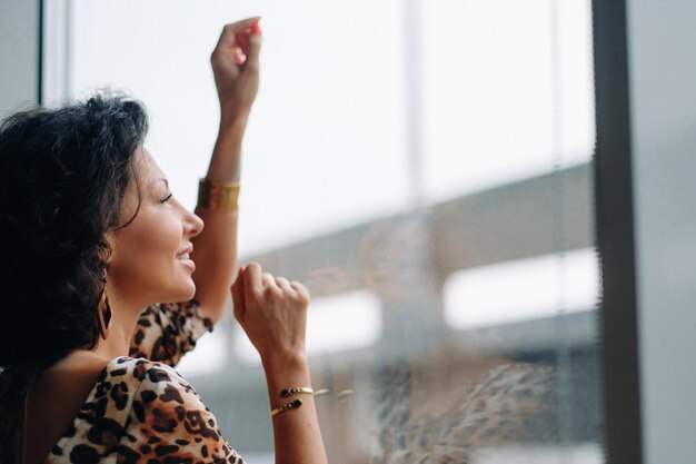 A brunette woman in a tiger dress stands near a large window