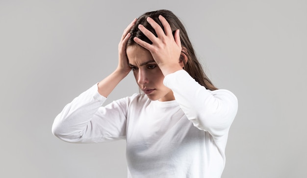 Brunette woman touching her temples feeling stress, on gray background. Woman suffering from headache desperate, stressed because pain and migraine. Woman with hard headache holding hands on head.