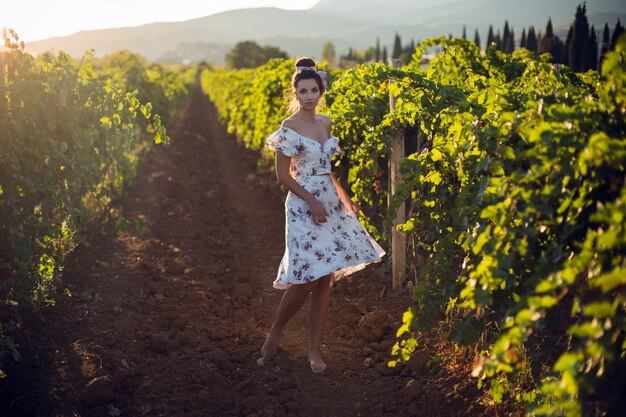 Брюнетка в белом платье стоит на винограднике летом в Италии