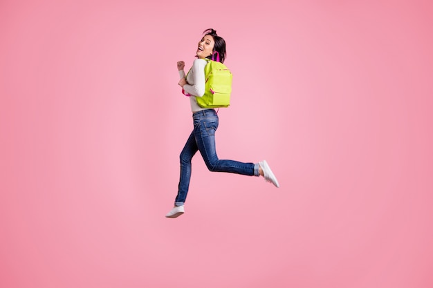 brunette woman in white pullover jumping with backpack isolated on pink