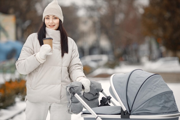 Brunette woman with baby stroller walking in the city with takeaway coffee