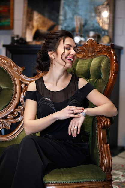 Brunette woman with hairstyle in black clothes sits on a sofa