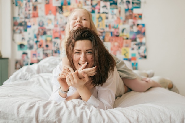 brunette woman with her beautiful happy daughter have fun  on bed