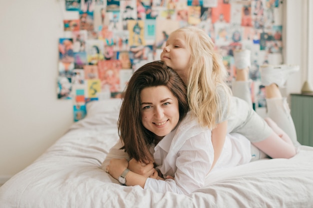 brunette woman with her beautiful happy daughter lying on bed