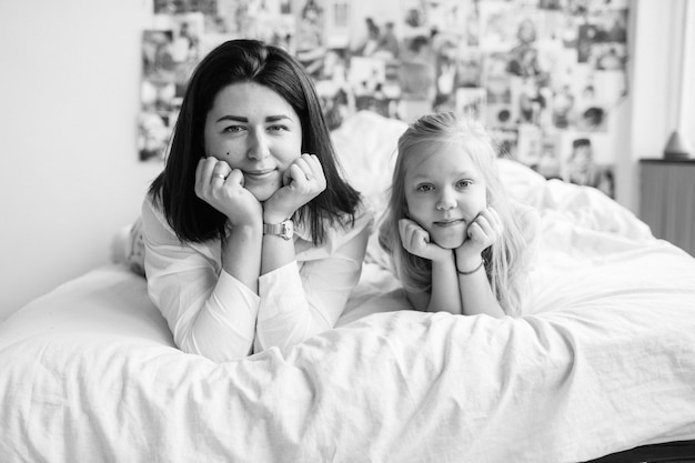 brunette woman with her beautiful happy daughter lying  on bed