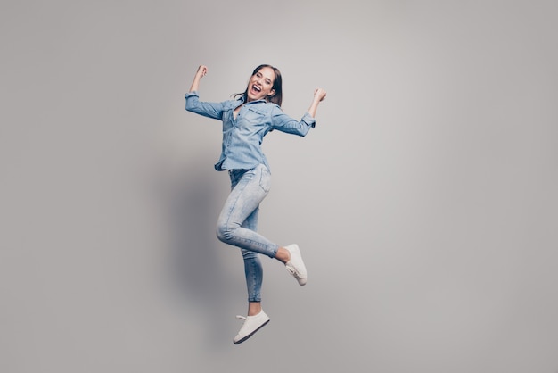 brunette woman with jeans jacket posing against the grey wall