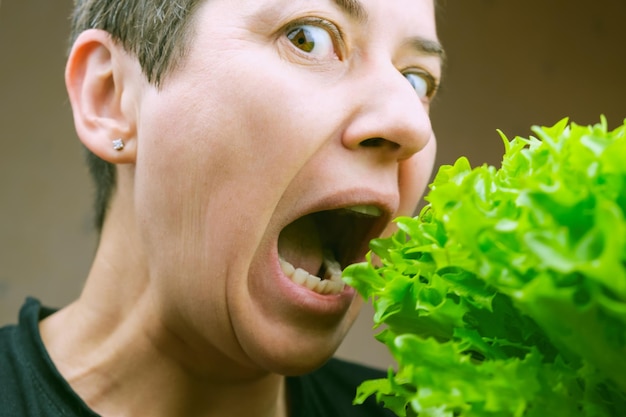 Foto una donna bruna con i capelli corti aprì la bocca per prendere un boccone di una rigogliosa insalata di lattuga biologica