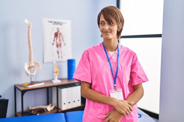 Brunette woman working at rehabilitation clinic looking away to side with smile on face, natural expression. laughing confident.