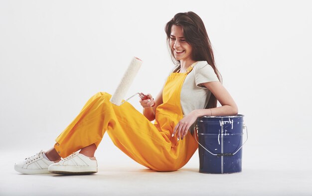 Brunette woman in yellow uniform sits against white wall in the studio