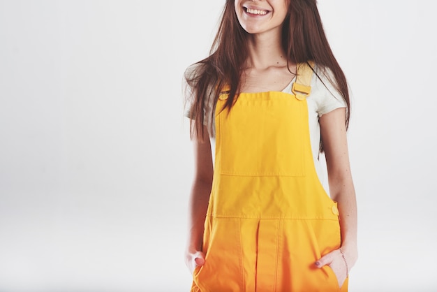 Brunette woman in yellow uniform stands against white wall in the studio