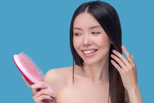 Brunette young asian woman holding a hairbrush and smiling