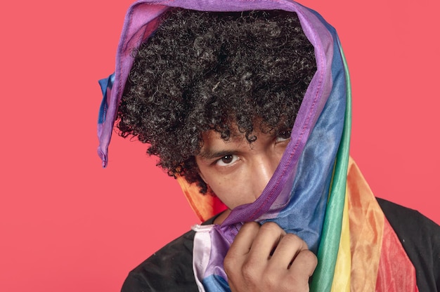 brunette young man with a LGBT flag over his head looking at the camera portrait view