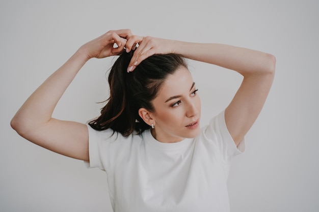 Brunette young woman making ponytail dressed in white tshirt Beautiful student preparing at home