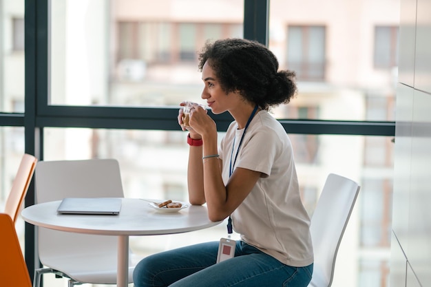 コーヒー ブレークを持つオフィスの食堂でブルネットの若い女性
