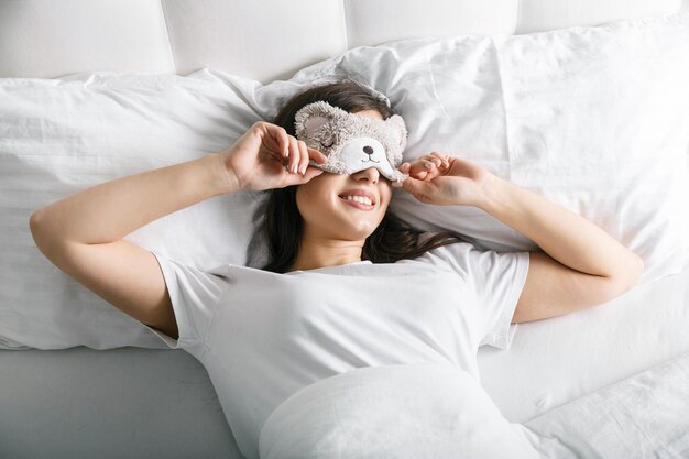 Brunnette vrouw in schattig teddy masker op gezicht wakker in haar slaapkamer