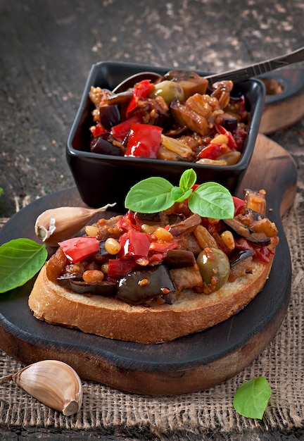 Bruschetta-caponata met rozijnen en pijnboompitten versierd met een blad van basilicum