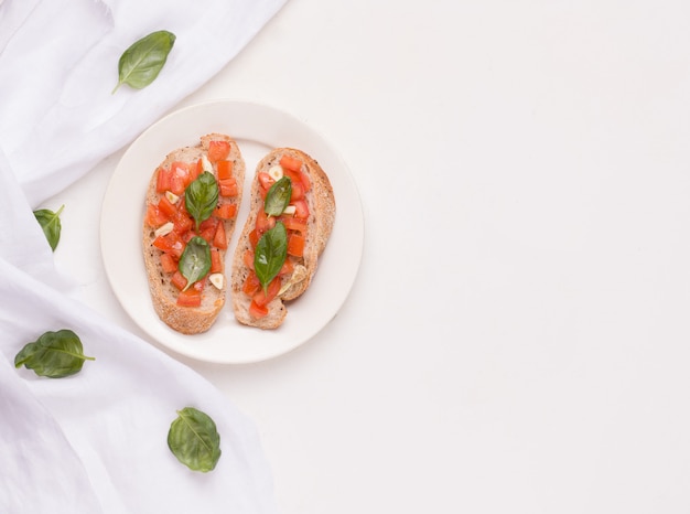 Bruschetta is a traditional Italian dish with tomato, garlic on a plate next to a cloth and basil leaves. copy space