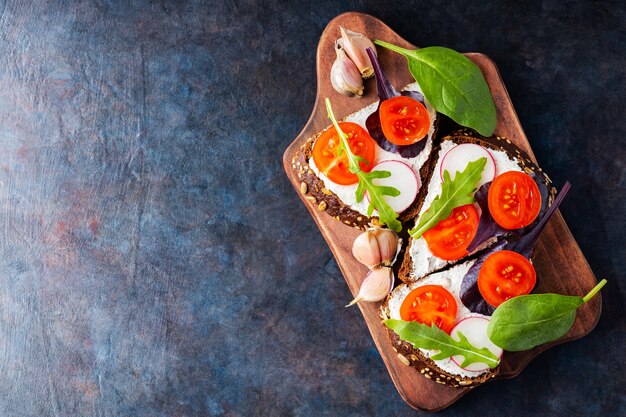 Bruschetta met roomkaas, cherrytomaatjes en knoflook op een snijplank. italiaanse antipasti bruschetta met roomkaas en verse kruiden. ruimte kopiëren. bovenaanzicht