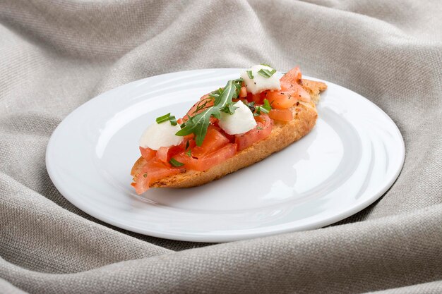 Bruschetta met tomaten en mozzarella op een witte plaat op een textielachtergrond