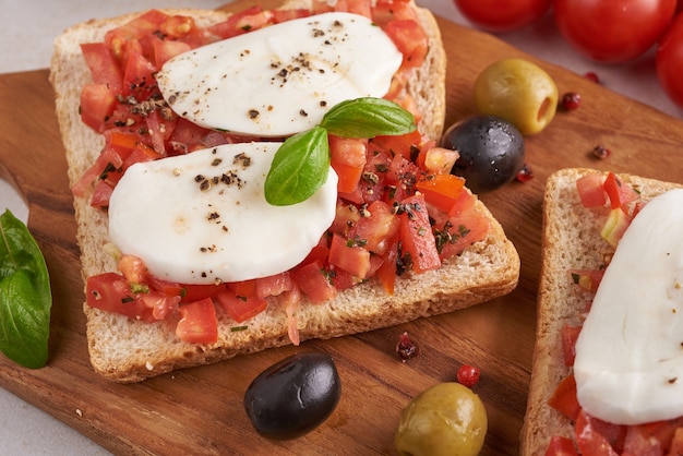 Bruschetta met tomaten, mozzarellakaas en basilicum op een snijplank. Traditioneel Italiaans voorgerecht of snack, antipasto. Caprese salade bruschetta. Bovenaanzicht met kopie ruimte. Plat leggen.