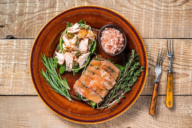 Bruschetta met warme en koude gerookte zalm, rucola, kappertjes op een rustieke plaat met kruiden. houten achtergrond. Bovenaanzicht.