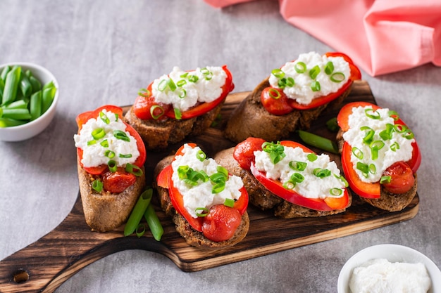 Bruschetta on rye bread with ricotta pepper tomato and green onion on the board