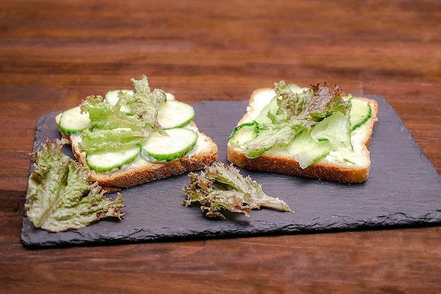 Bruschetta sandwich bread toast with soft green avocado cheese ricottafresh cucumbersbasil greenery on wooden cutting boardTasty healthy vegetarian foodItalian cuisine appetizertop view flat lay